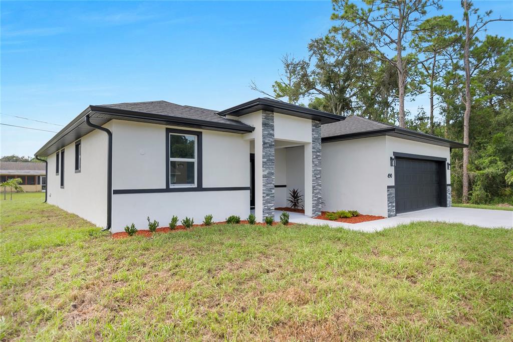 A modern, single-story house with white stucco walls, dark trim, and a stone-accented entryway — 490 CAROLINA AVENUE NW, PALM BAY, FL