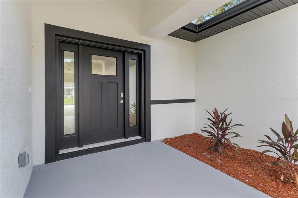 A black front door with side windows sits on a gray porch with two small plants — 490 CAROLINA AVENUE NW, PALM BAY, FL