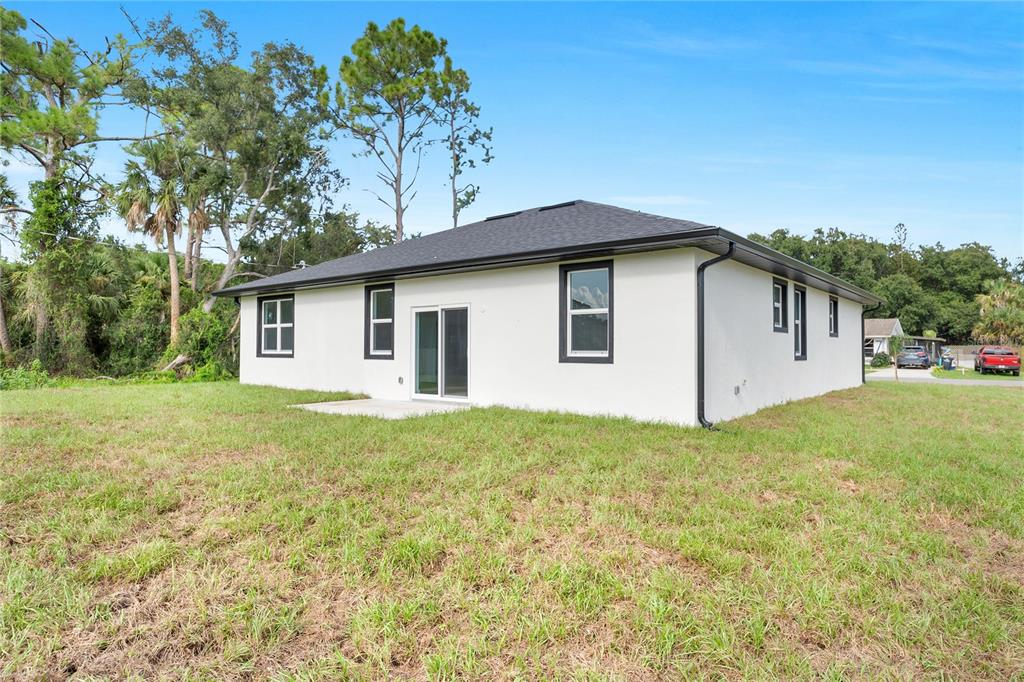 The rear exterior of a white stucco house features a small concrete patio and lawn — 490 CAROLINA AVENUE NW, PALM BAY, FL