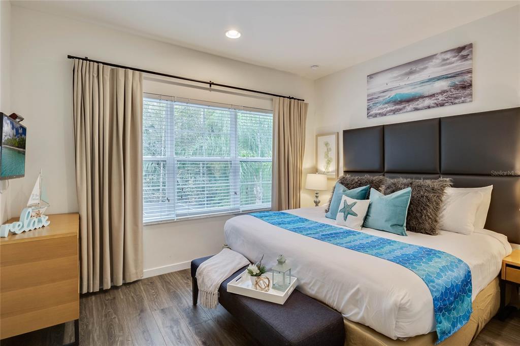 A bedroom features a king bed with a blue runner, dark headboard, and wood flooring — 5710 OLGA STREET, KISSIMMEE, FL