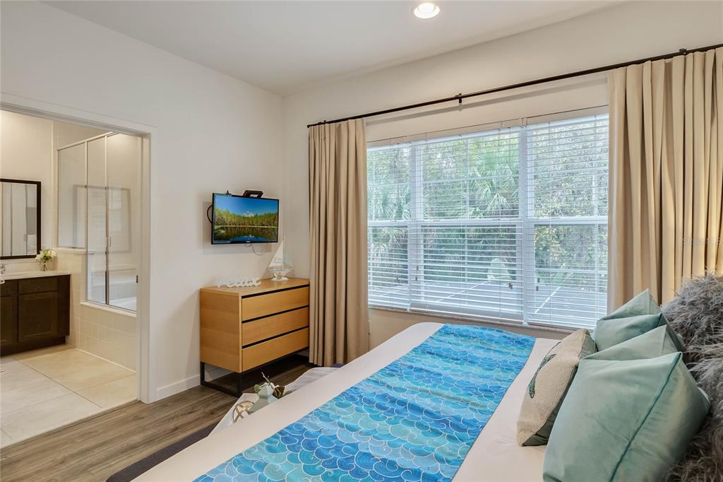A bedroom with a dresser, wall-mounted television, and an attached bathroom with a glass shower — 5710 OLGA STREET, KISSIMMEE, FL