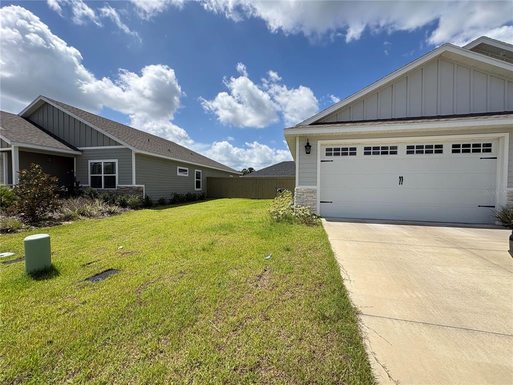 A grassy side yard sits between two suburban houses with light-colored siding and garages — 6737 SW 13TH LANE, GAINESVILLE, FL