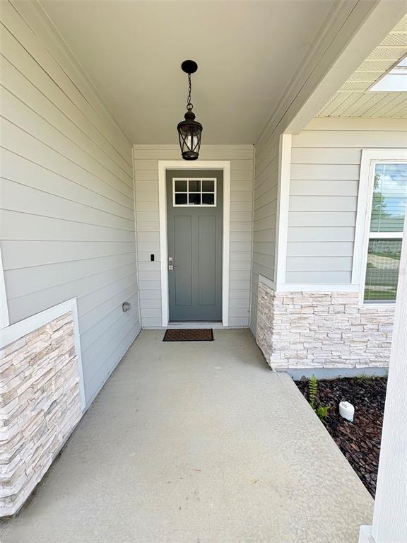 A covered front porch features light gray siding, stone accents, and a dark gray door — 6737 SW 13TH LANE, GAINESVILLE, FL