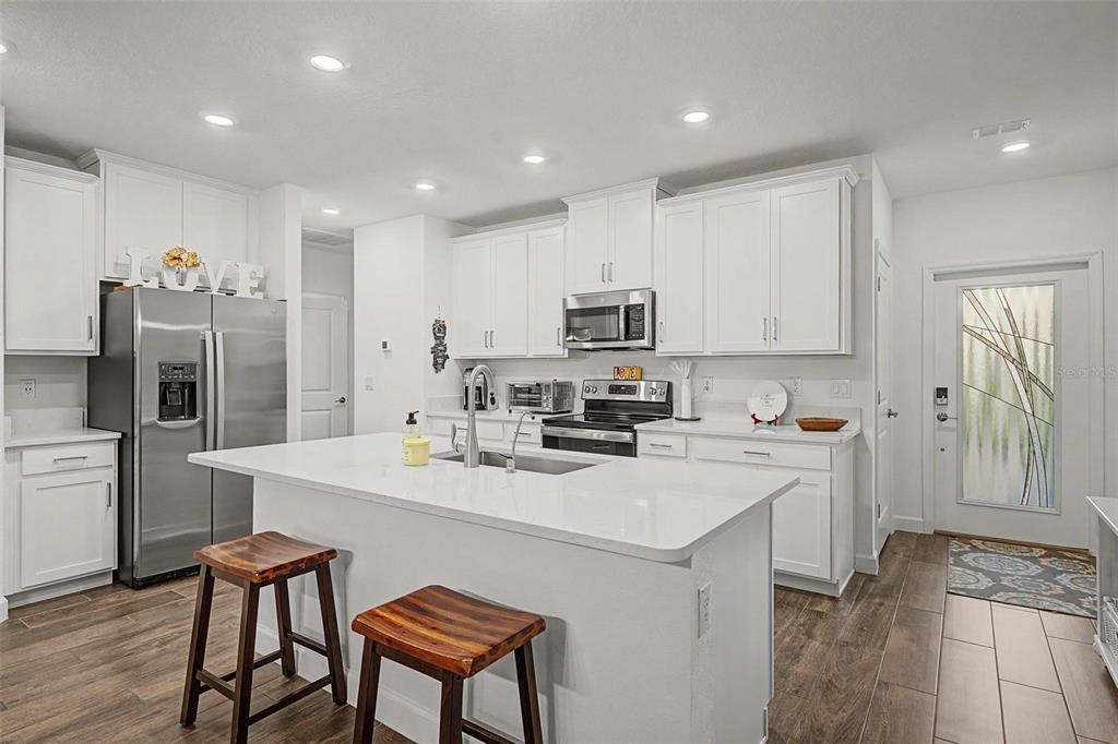 A modern kitchen features white cabinetry, a central island with bar stools, and stainless appliances — 32172 CANNON RUSH DRIVE, SAN ANTONIO, FL