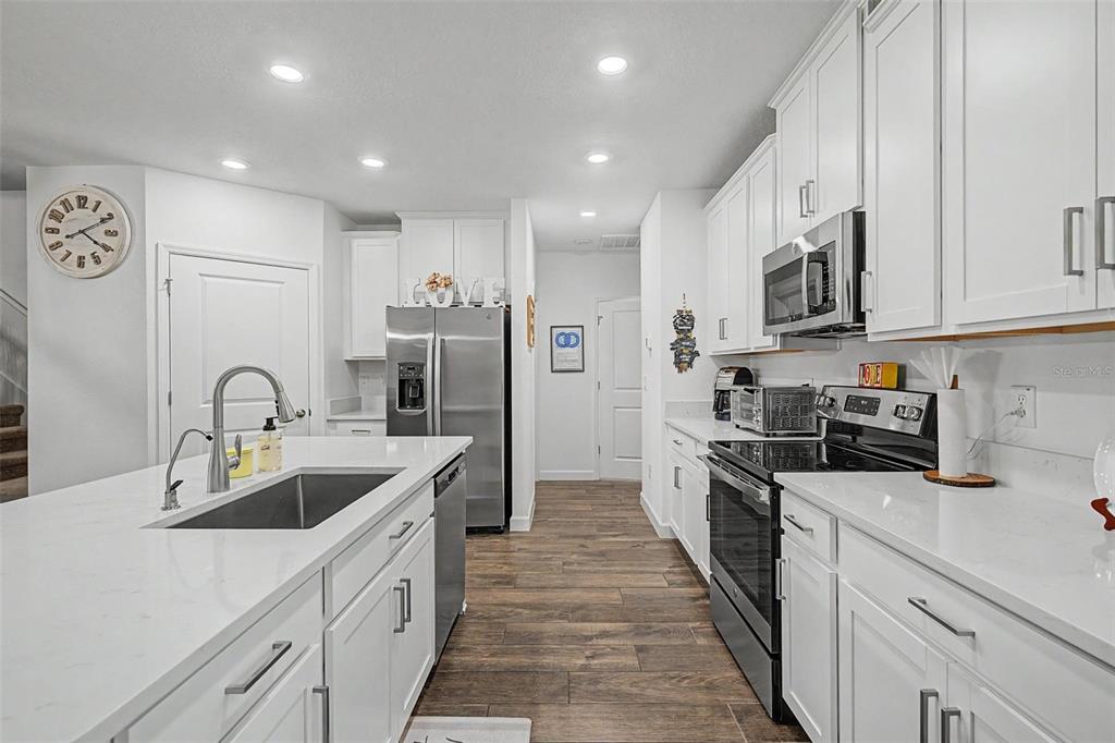 A modern kitchen features white cabinets, stainless steel appliances, a large island, and wood-look flooring — 32172 CANNON RUSH DRIVE, SAN ANTONIO, FL