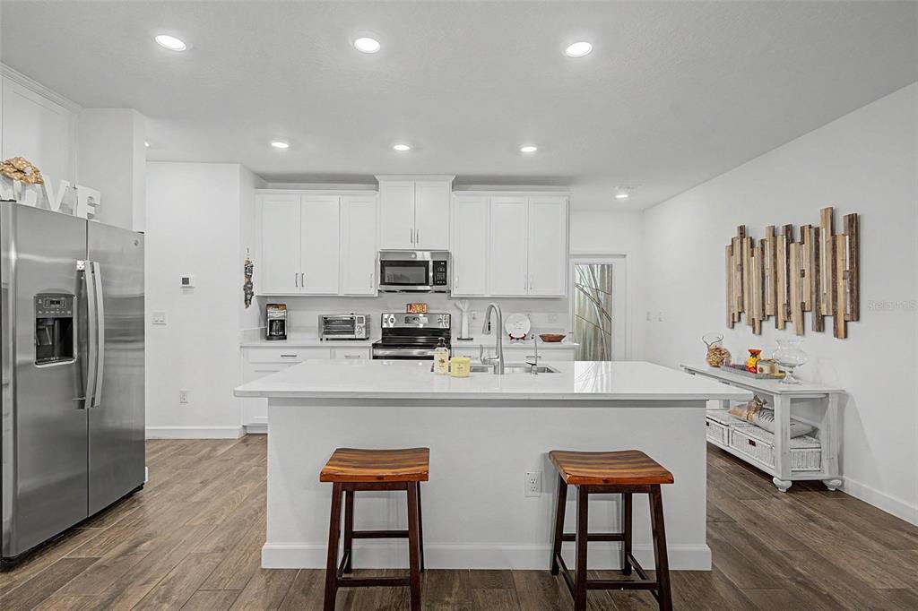A modern kitchen features white cabinetry, a central island with two stools, and stainless appliances — 32172 CANNON RUSH DRIVE, SAN ANTONIO, FL