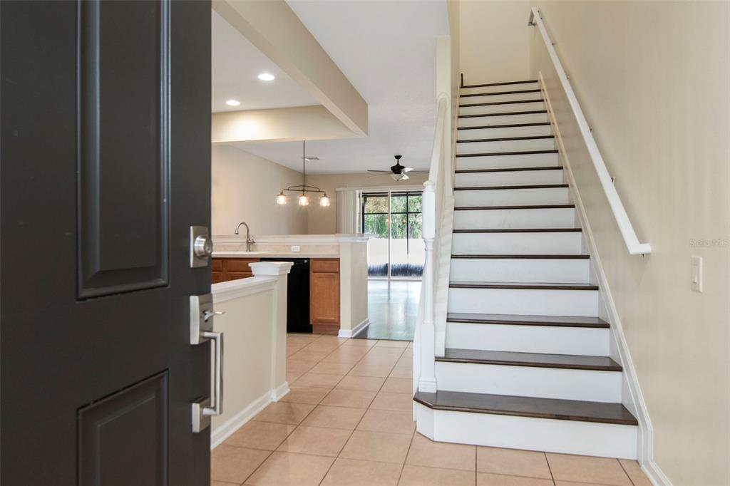 An entryway with tile flooring, a staircase with dark treads, and a view of the kitchen — 10208 ESTERO BAY LANE, TAMPA, FL