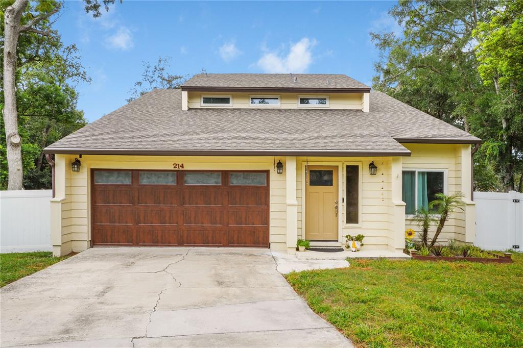 A yellow house with a brown garage door, a front door, and a dormer window — 214 PEMBROOK PLACE, LONGWOOD, FL