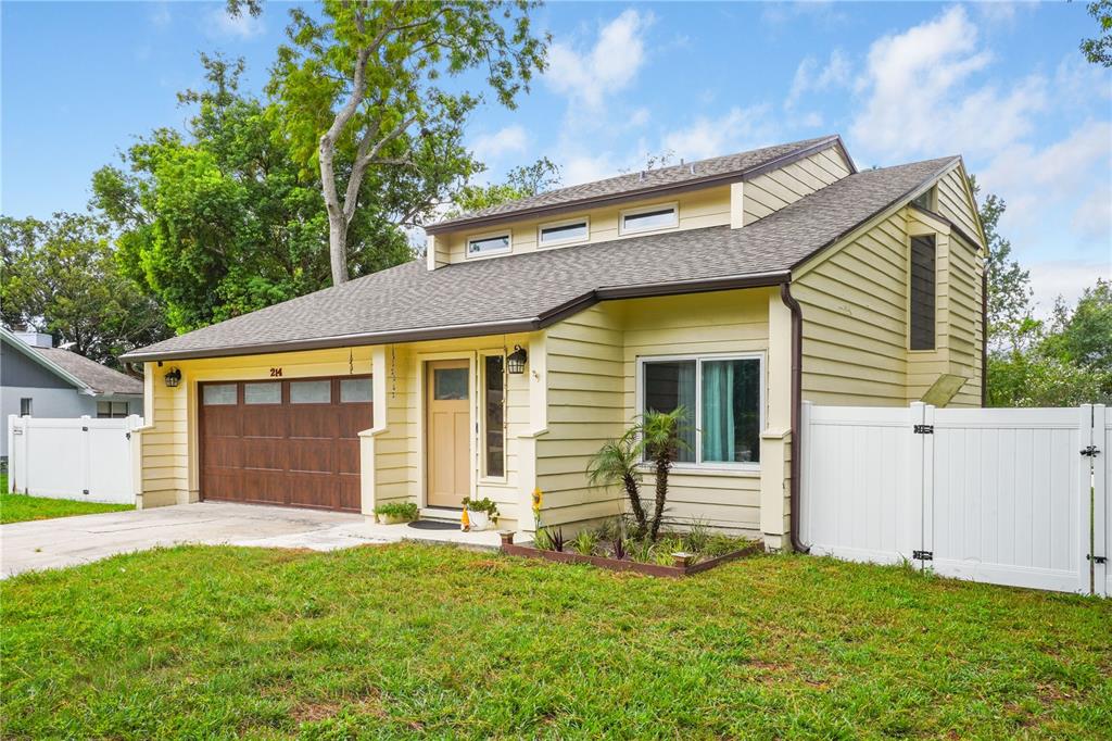 A yellow house with a brown garage door and a white vinyl fence — 214 PEMBROOK PLACE, LONGWOOD, FL