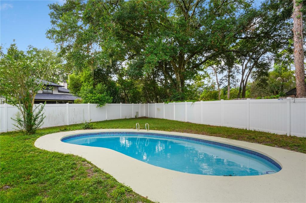 A backyard features a kidney-shaped swimming pool surrounded by a white vinyl fence and trees — 214 PEMBROOK PLACE, LONGWOOD, FL