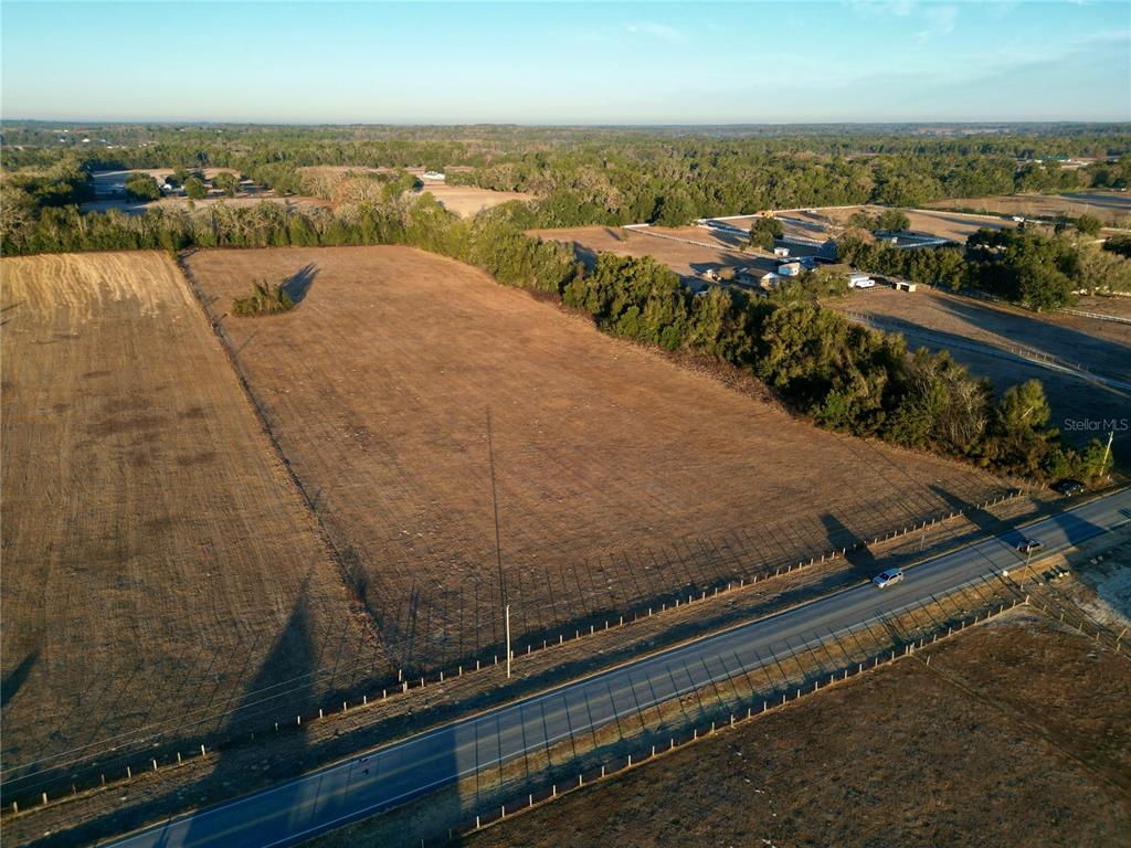An aerial view shows a large, rectangular, dry grassy field bordered by a road and trees — TBD NW HWY 225A, OCALA, FL