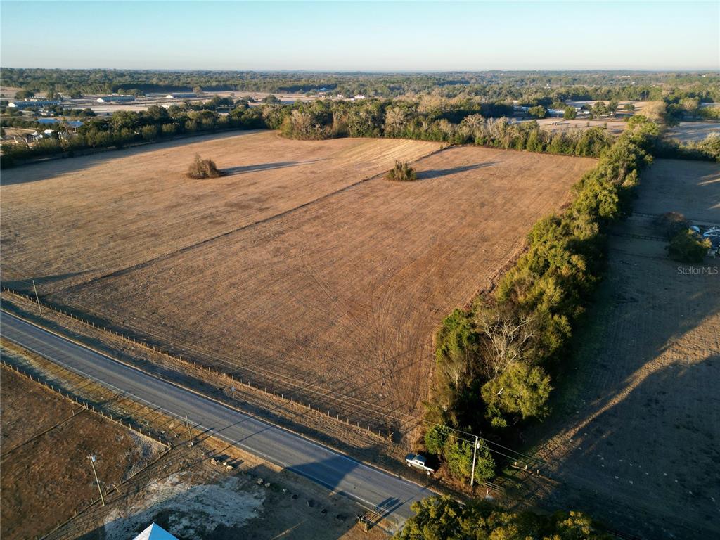 An aerial view shows a large, dry, open field bordered by trees and a road — TBD NW HWY 225A, OCALA, FL