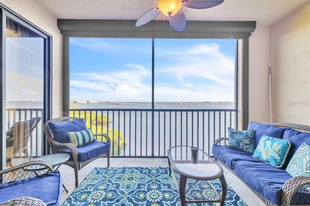 A screened-in balcony features blue wicker furniture, a patterned rug, and a waterfront view — 900 E MARION AVENUE UNIT 1310, PUNTA GORDA, FL