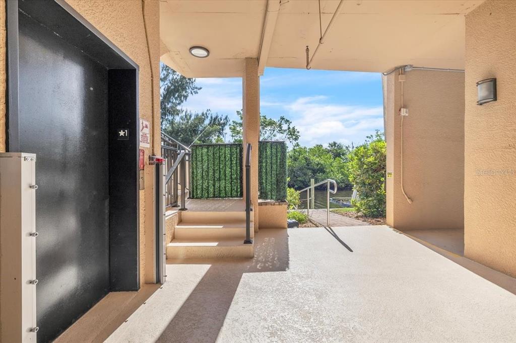 An outdoor covered walkway leads to an elevator and stairs overlooking a canal and greenery — 900 E MARION AVENUE UNIT 1310, PUNTA GORDA, FL