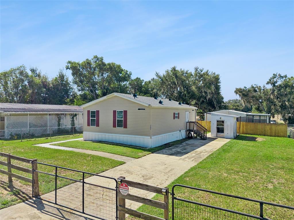 A tan manufactured home with a concrete driveway and a fenced yard under a blue sky — 17537 PALM DR, MONTVERDE, FL