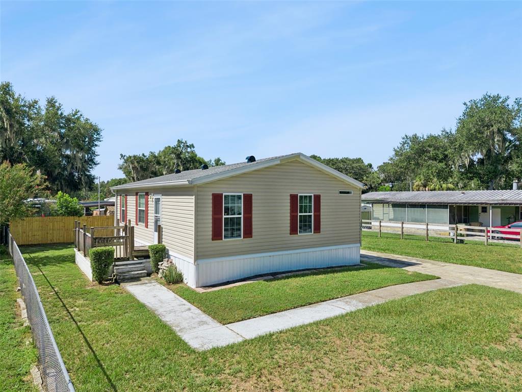A tan manufactured home with red shutters sits on a grassy lot with a deck — 17537 PALM DR, MONTVERDE, FL