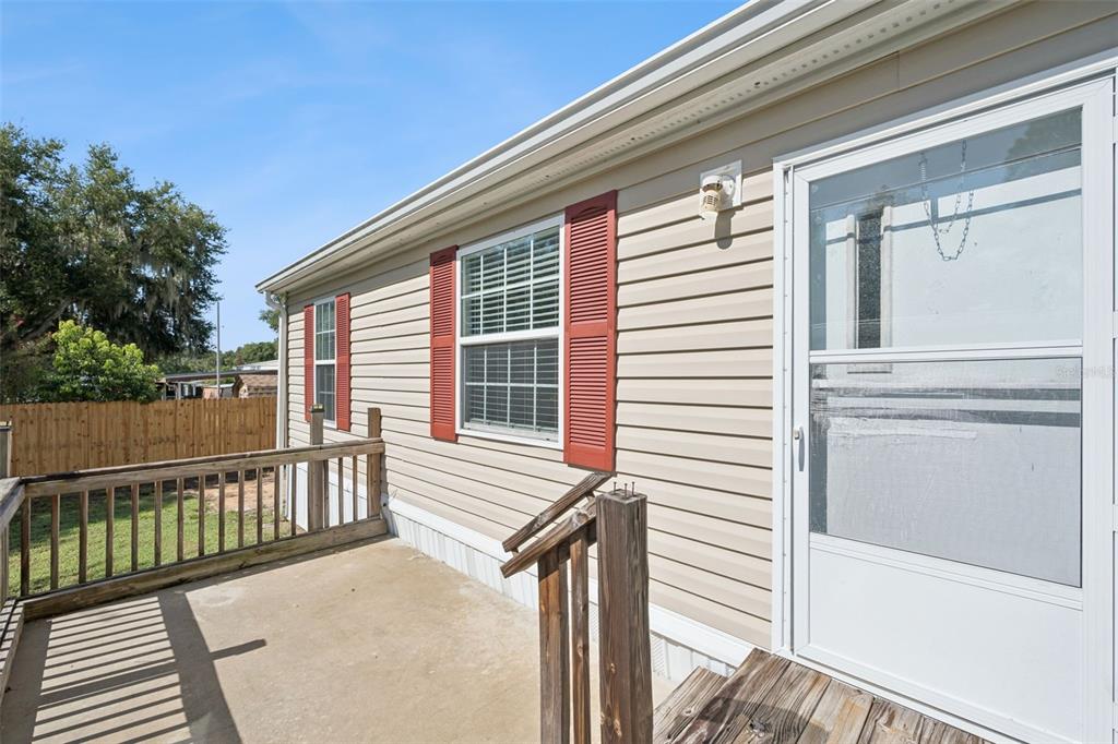 A beige vinyl-sided house exterior features a concrete porch, wooden railings, and red window shutters — 17537 PALM DR, MONTVERDE, FL