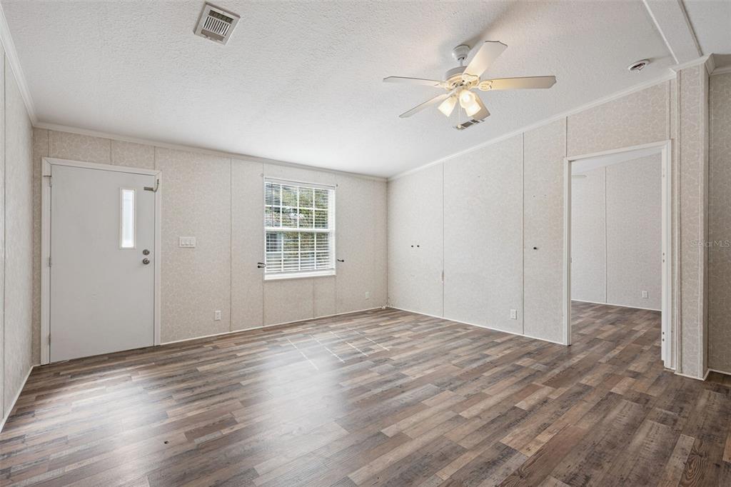 An empty room features wood-look flooring, light-colored panel walls, a ceiling fan, and a window — 17537 PALM DR, MONTVERDE, FL