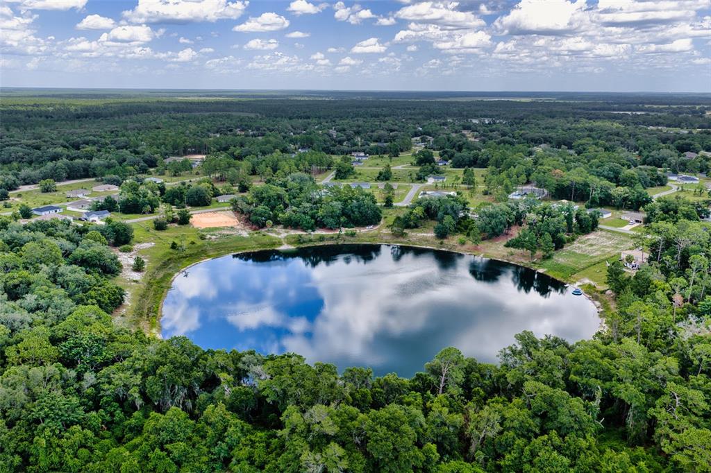 An aerial view shows a circular lake surrounded by dense trees and nearby residential houses — MALAUKA LOOP, OCKLAWAHA, FL