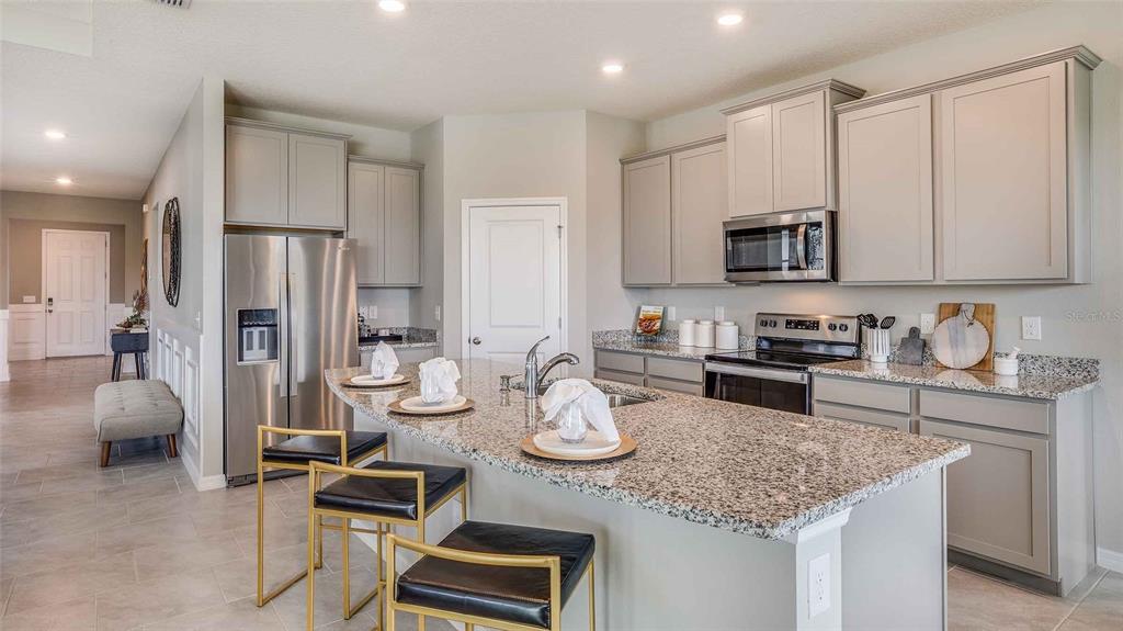A kitchen features gray cabinets, granite countertops, a stainless steel refrigerator, and a breakfast island — 32668 DULUTH DRIVE, WESLEY CHAPEL, FL