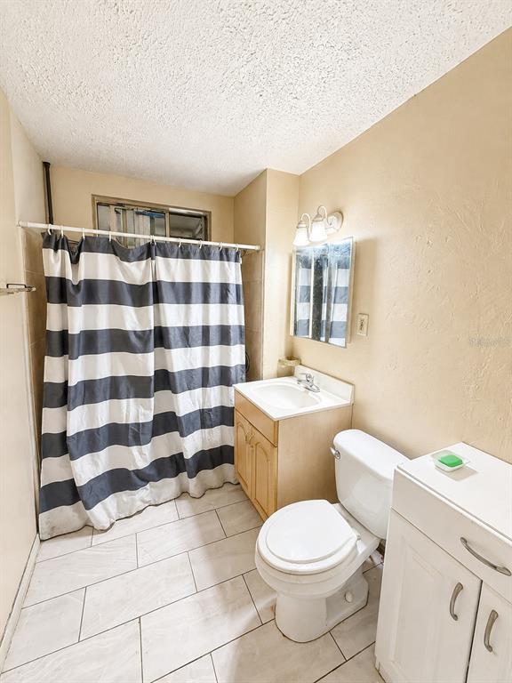 A bathroom features a striped shower curtain, a vanity, a toilet, and light-colored tile flooring — 202 SHADY PLACE, DAYTONA BEACH, FL