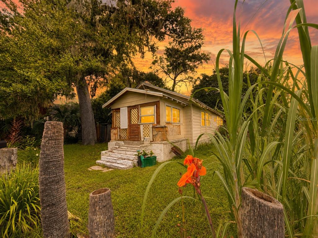A small, light-colored cottage with a front porch sits on a grassy lot at sunset — 202 SHADY PLACE, DAYTONA BEACH, FL
