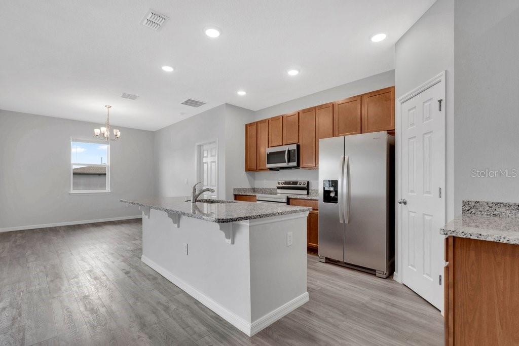 A kitchen with wood cabinets, stainless steel appliances, and a granite-topped island on gray flooring — 30502 PINTAIL DRIVE, LEESBURG, FL