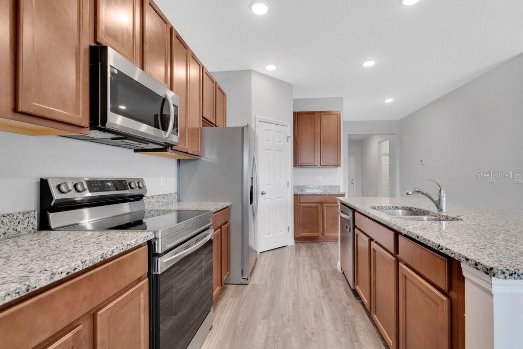 A kitchen features wood cabinets, granite countertops, stainless steel appliances, and light wood-look flooring — 30502 PINTAIL DRIVE, LEESBURG, FL