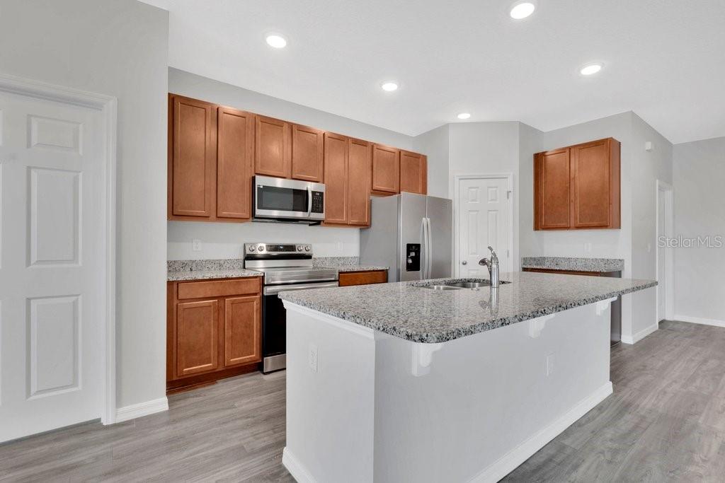A kitchen with wood cabinets, granite countertops, a center island, and stainless steel appliances — 30502 PINTAIL DRIVE, LEESBURG, FL