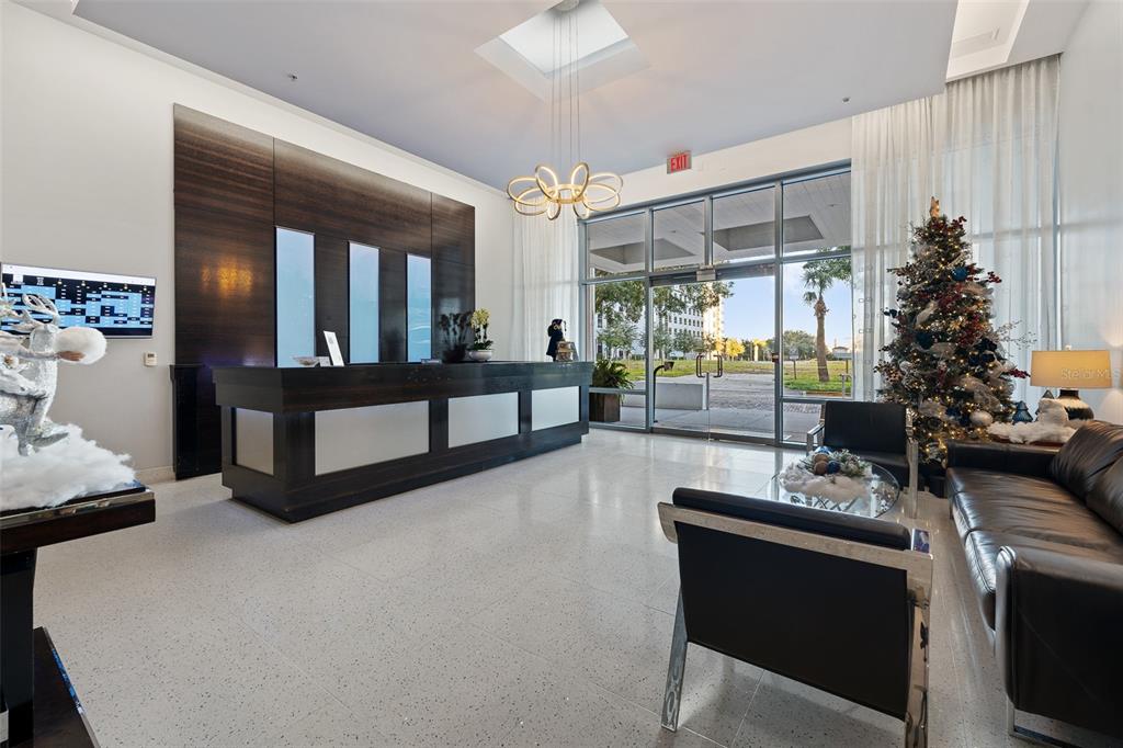 A modern lobby features a dark wood reception desk, a Christmas tree, and glass doors — 260 S OSCEOLA AVENUE UNIT 1203, ORLANDO, FL