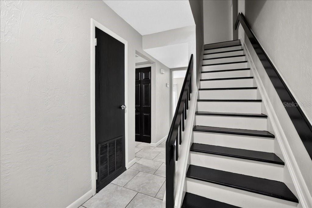 A staircase with black treads and white risers sits beside a hallway with tiled floors — 5 GLEN ARBOR PARK, ORMOND BEACH, FL