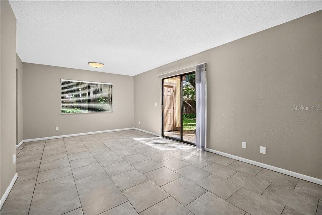 An empty living room features light gray walls, large floor tiles, and a sliding glass door — 5 GLEN ARBOR PARK, ORMOND BEACH, FL