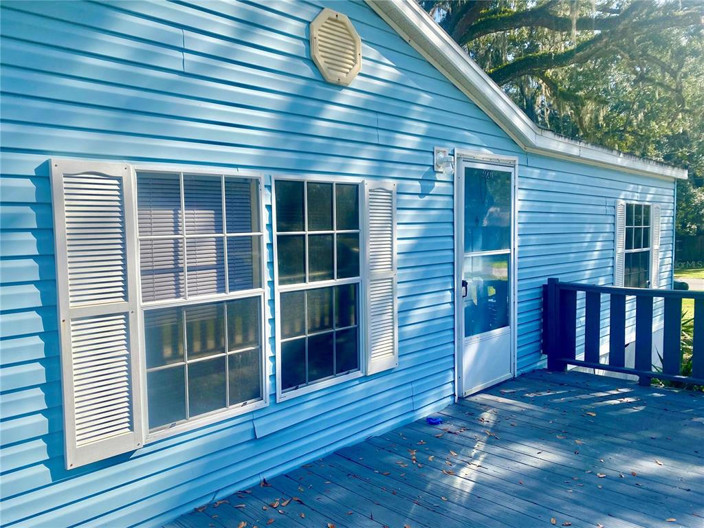 A light blue house exterior features a wooden deck, white-trimmed windows, and a screen door — 9220 DAN LYNN STREET, BROOKSVILLE, FL