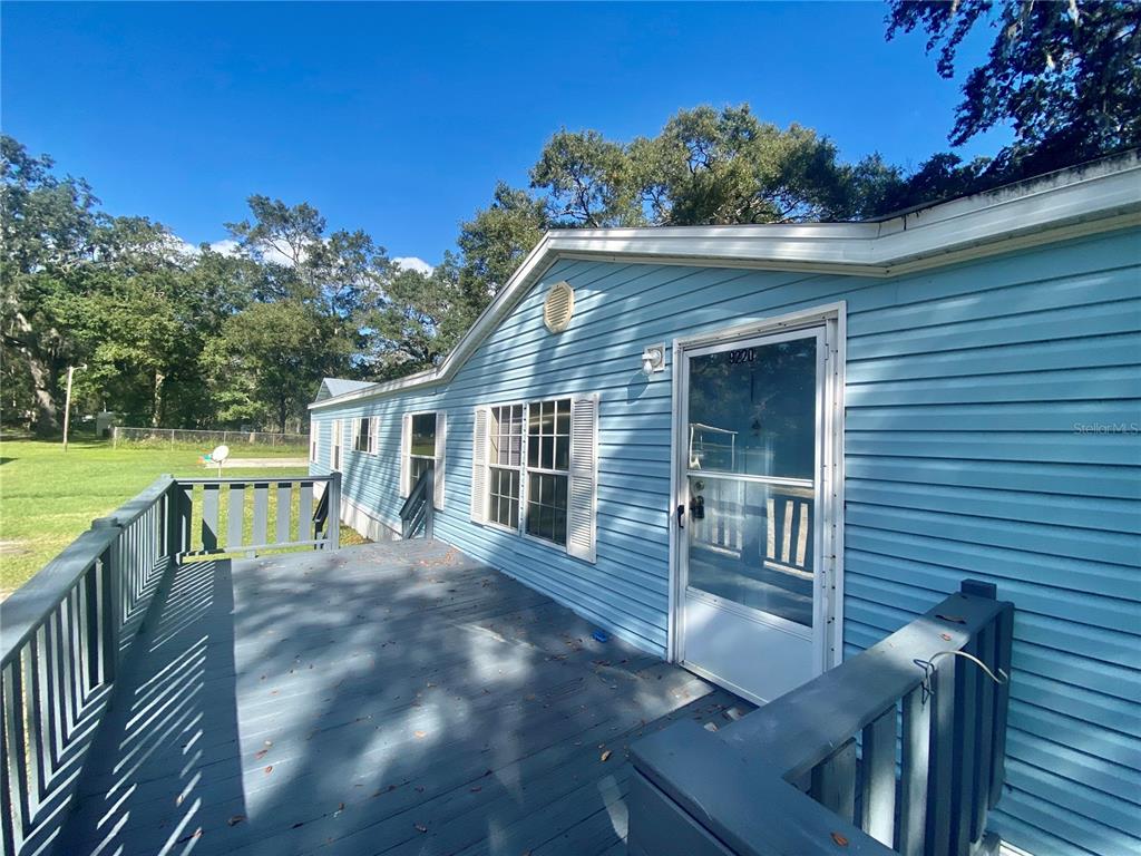 A light blue house with horizontal siding features a large wooden deck and front door — 9220 DAN LYNN STREET, BROOKSVILLE, FL