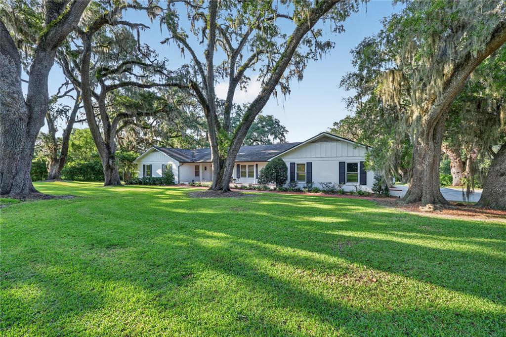 A single-story white house with dark shutters sits on a large lawn under mature trees — 1311 SE 17TH AVENUE, OCALA, FL