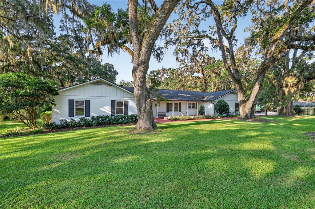 A white single-story house with black shutters sits on a grassy lawn under large trees — 1311 SE 17TH AVENUE, OCALA, FL