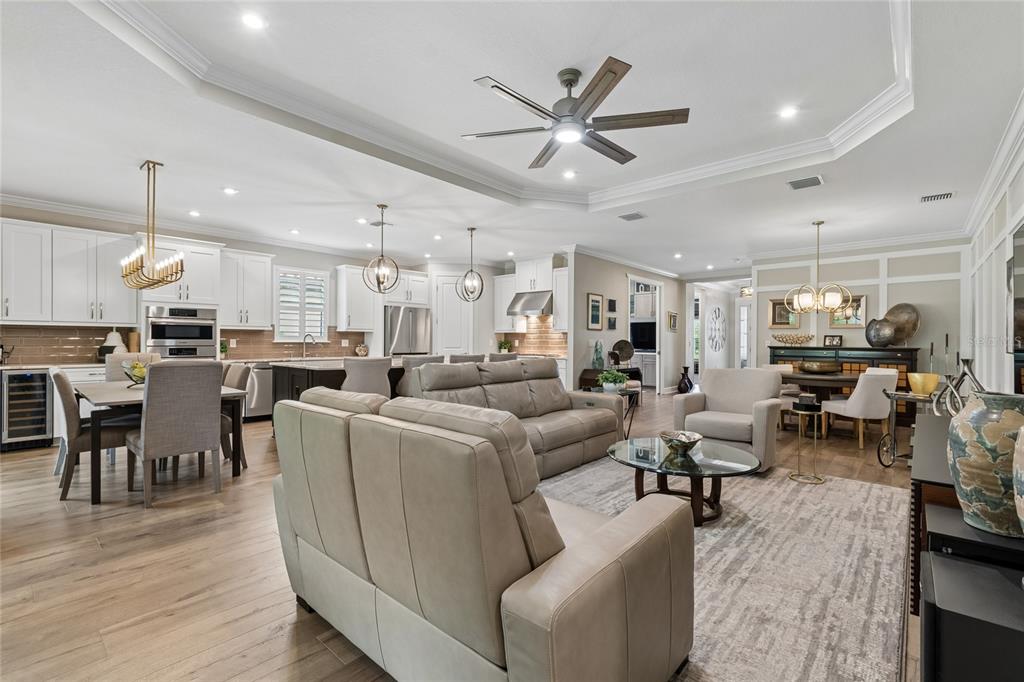 An open-concept living room and kitchen featuring light wood floors, neutral furniture, and tray ceilings — 29534 GINNETTO DRIVE, WESLEY CHAPEL, FL