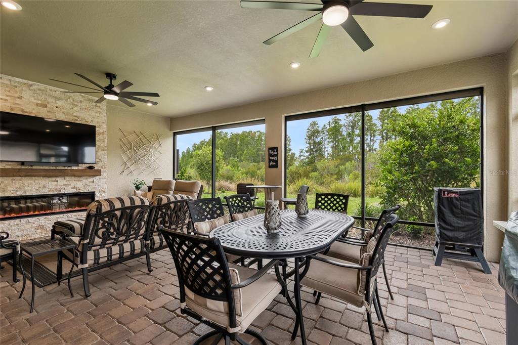 A covered patio features a stone fireplace, outdoor furniture, and large screened windows overlooking greenery — 29534 GINNETTO DRIVE, WESLEY CHAPEL, FL