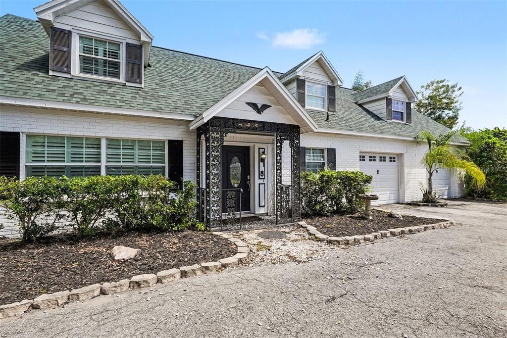 A white brick house features a green shingled roof, dormer windows, and a decorative metal porch — 404 CLARISSA DRIVE, BRANDON, FL