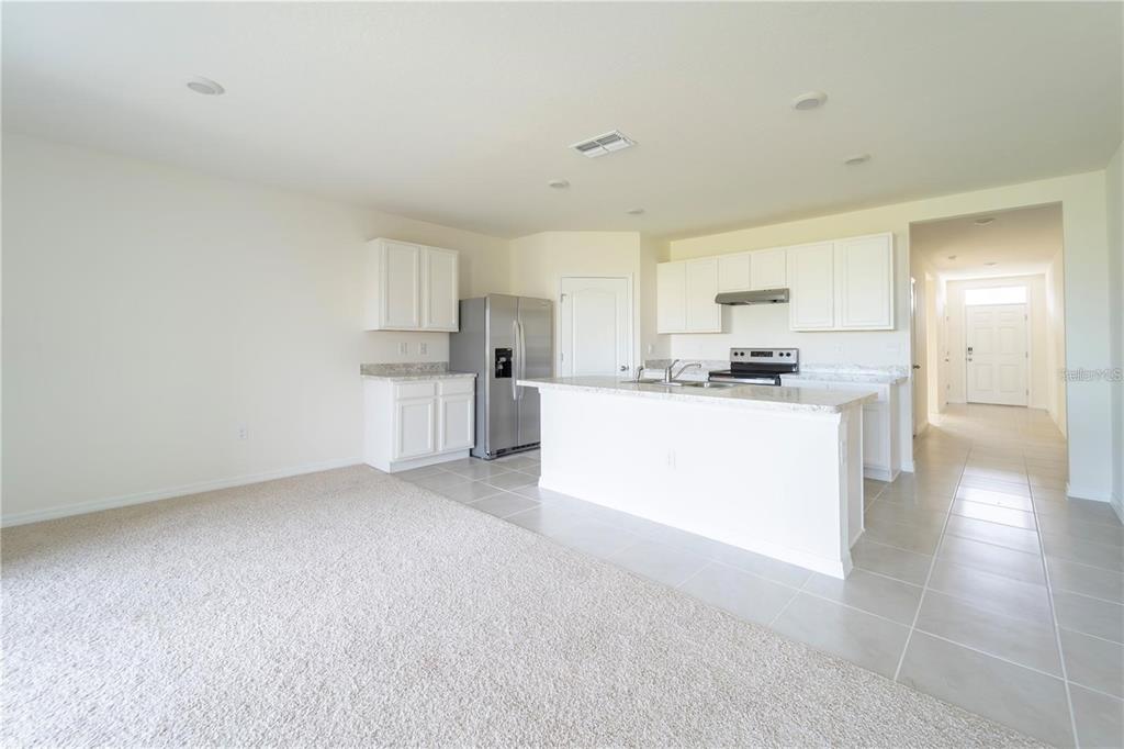 A kitchen with white cabinets, stainless steel appliances, and an island overlooks a carpeted area — 1811 SILVERBELL LOOP, HAINES CITY, FL