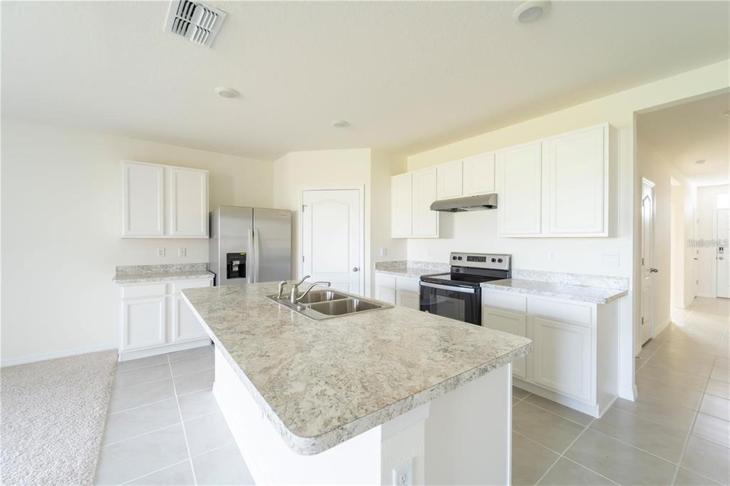 A kitchen features white cabinets, granite countertops, a center island, and stainless steel appliances — 1811 SILVERBELL LOOP, HAINES CITY, FL