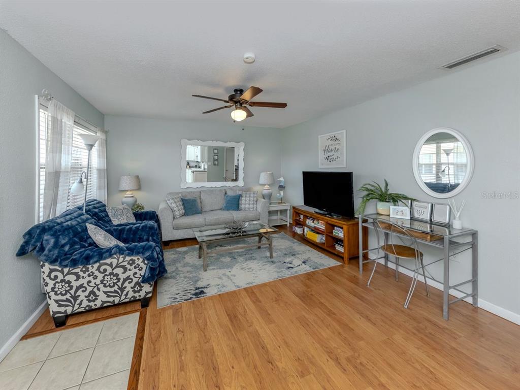 A living room features light blue walls, wood-look flooring, a sofa, and a television console — 400 BASE AVENUE E UNIT 227, VENICE, FL