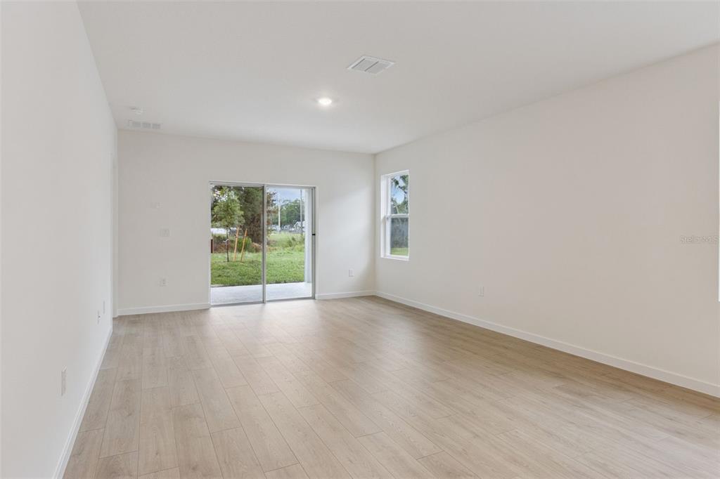 An empty room features light wood-look flooring, white walls, a sliding glass door, and windows — 1347 GRAND FLORA LANE, SANFORD, FL