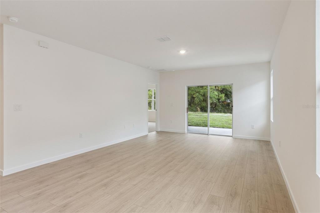 An empty living room with light wood-look flooring, white walls, and a sliding glass door — 1347 GRAND FLORA LANE, SANFORD, FL