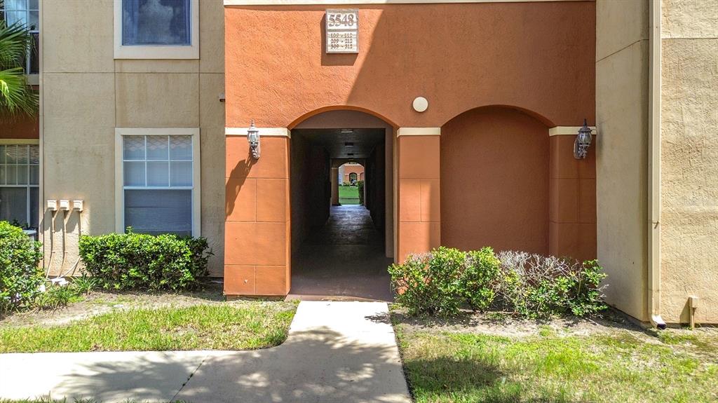 An exterior view of an apartment building entrance with a walkway leading through the center — 5548 METROWEST BOULEVARD UNIT 209, ORLANDO, FL