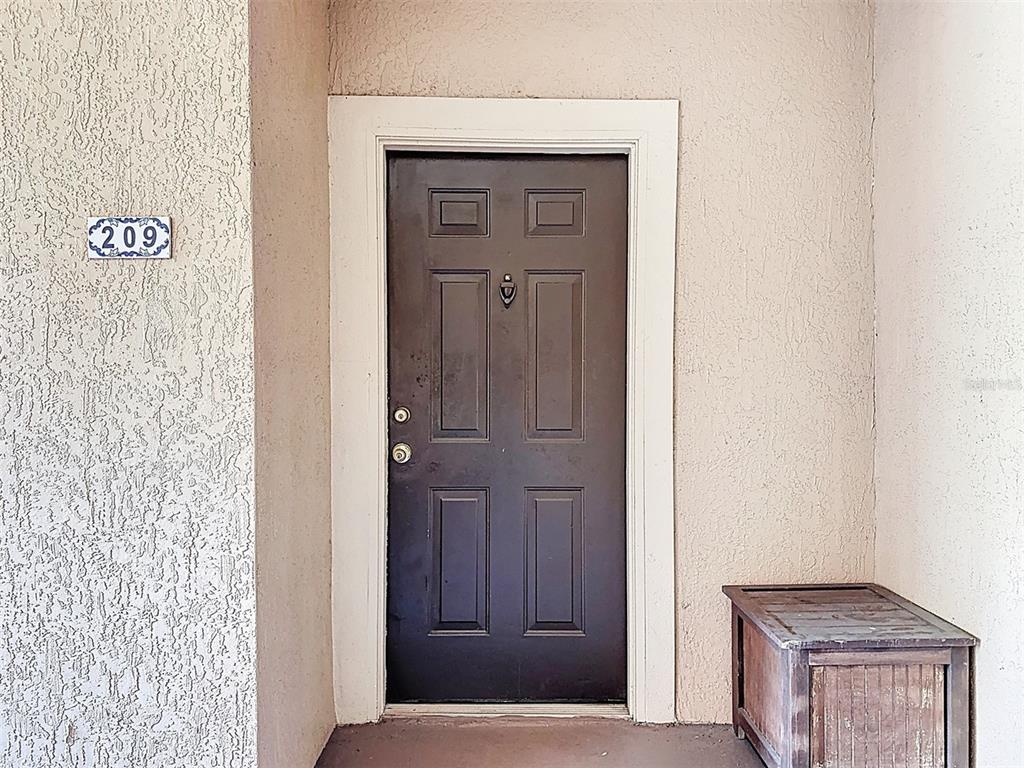 A dark brown front door with a door knocker is set in a beige wall — 5548 METROWEST BOULEVARD UNIT 209, ORLANDO, FL