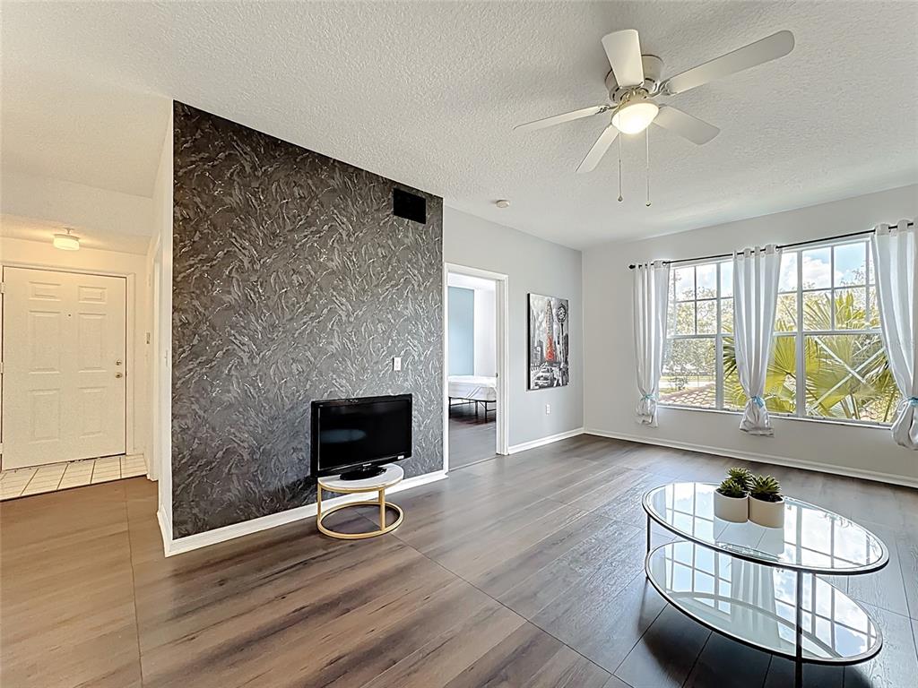 A living room features dark wood-look flooring, a textured accent wall, and a ceiling fan — 5548 METROWEST BOULEVARD UNIT 209, ORLANDO, FL