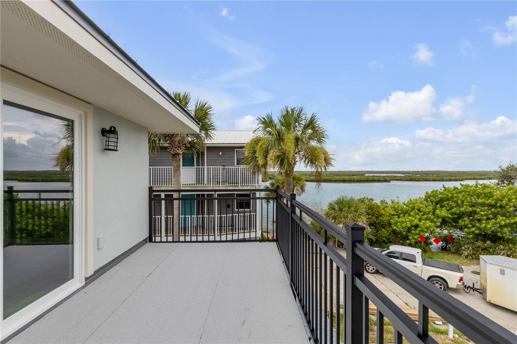 An elevated balcony with black railings overlooks a body of water and a parking area — 830 EEL AVENUE, NEW SMYRNA BEACH, FL