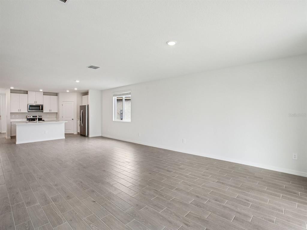An open-concept living area features gray wood-look tile flooring and a kitchen with white cabinets — 7214 RAY CREEK DRIVE, BROOKSVILLE, FL