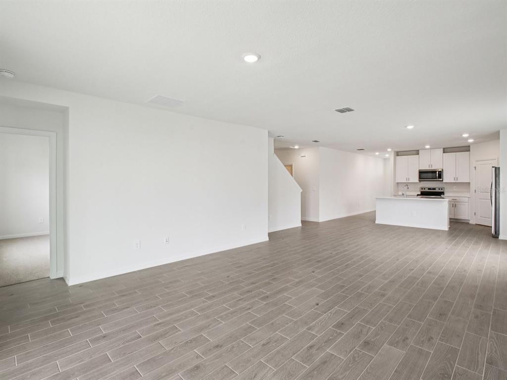 An open-concept living area features gray wood-look tile flooring and a kitchen with white cabinetry — 7214 RAY CREEK DRIVE, BROOKSVILLE, FL